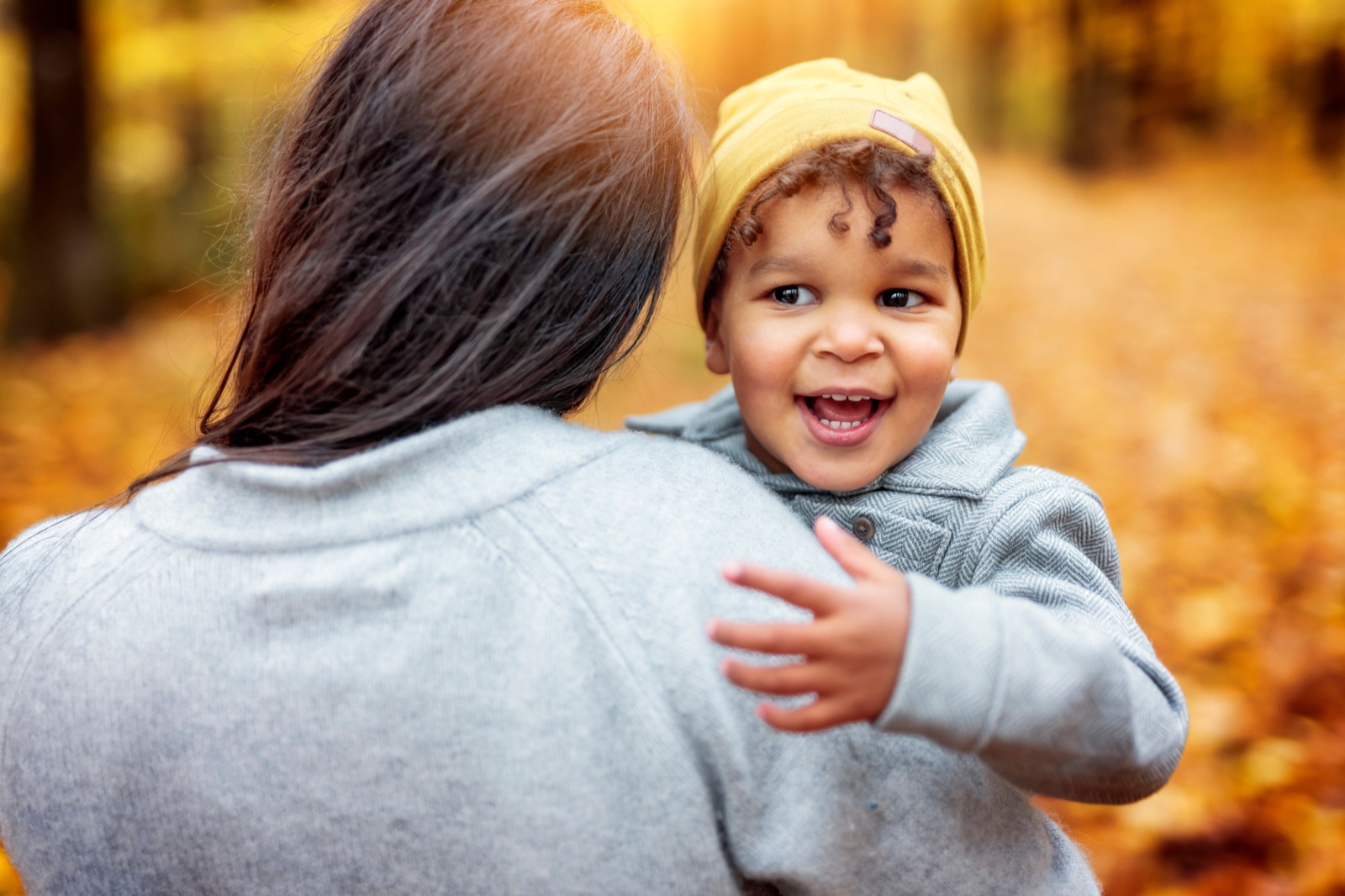 A smiling child held by his mother outdoors
